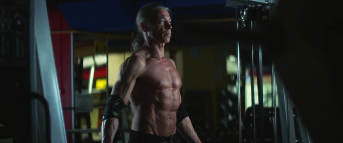 Middle aged muscular man with long gray ponytail works out in the gym