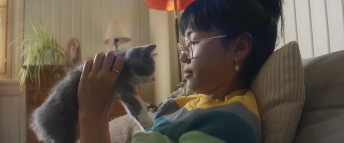 Asian teenager girl sitting at the couch holding and petting and kissing a little kitten