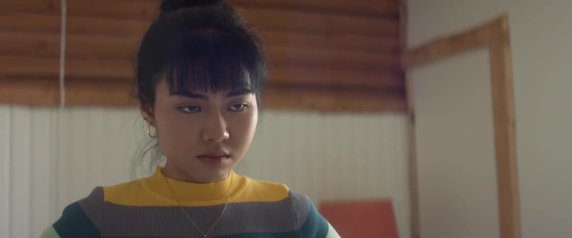 A teenage girl removes her arm that is wrapped over her body and with a frown on her face runs her hands over her breasts