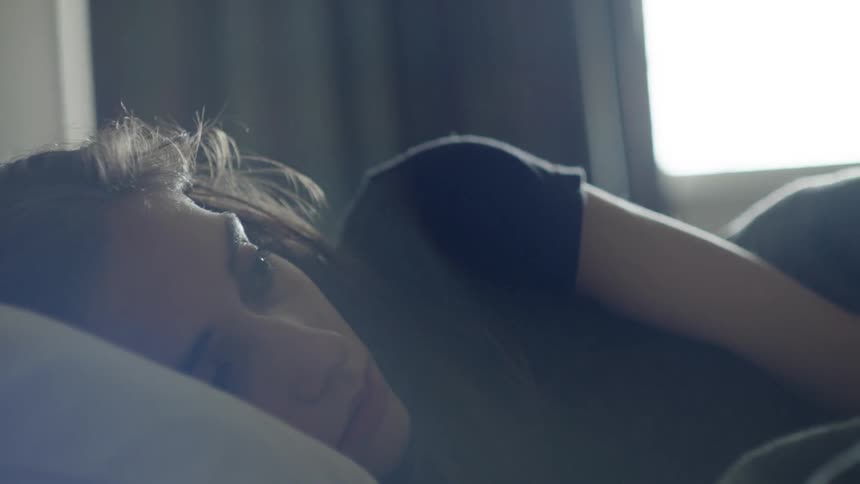 A woman is sleeping in bed as light shines in the window