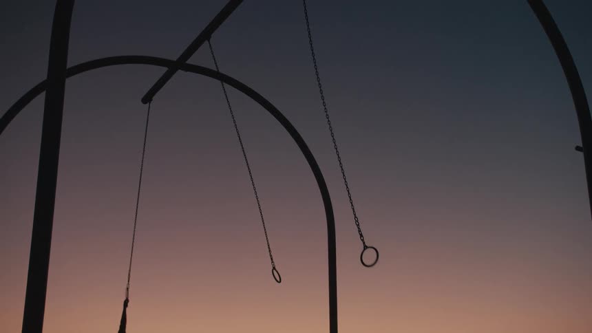 A woman swings across monkey bars at a playground before falling