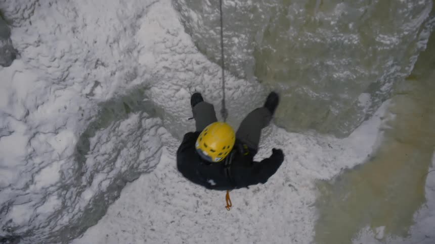 A rock climber descends a snowy rockface using a rope and a harness