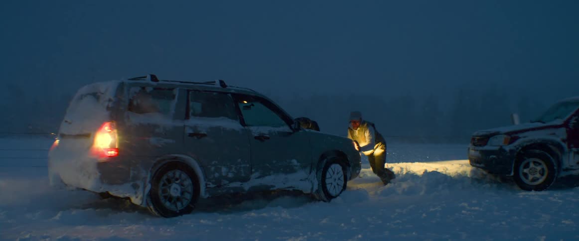 Two men push a vehicle out of the deep snow at night