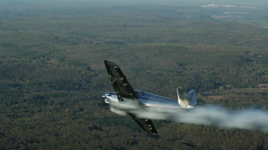 A man is flying a small airplane over a forest and the airplane is smoking as it turns