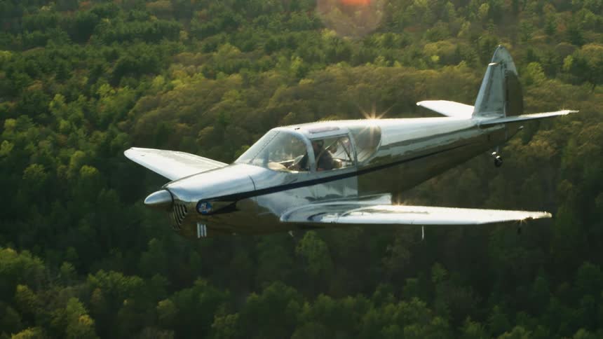 A man is flying a small airplane over a forest