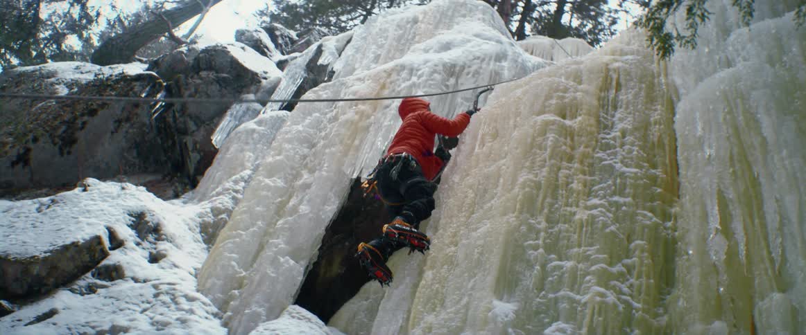 A person uses a large hook to climb up an ice covered mountain