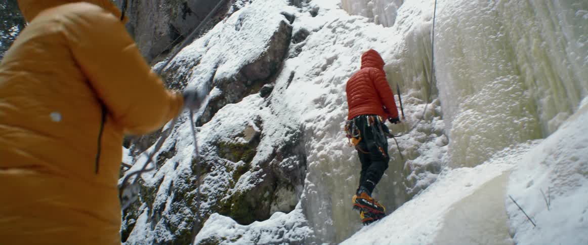A person pulls a rope pulley for another person rock climbing a snow covered mountain