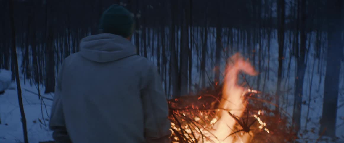 A man watches an outdoor fire in a wooded area at night