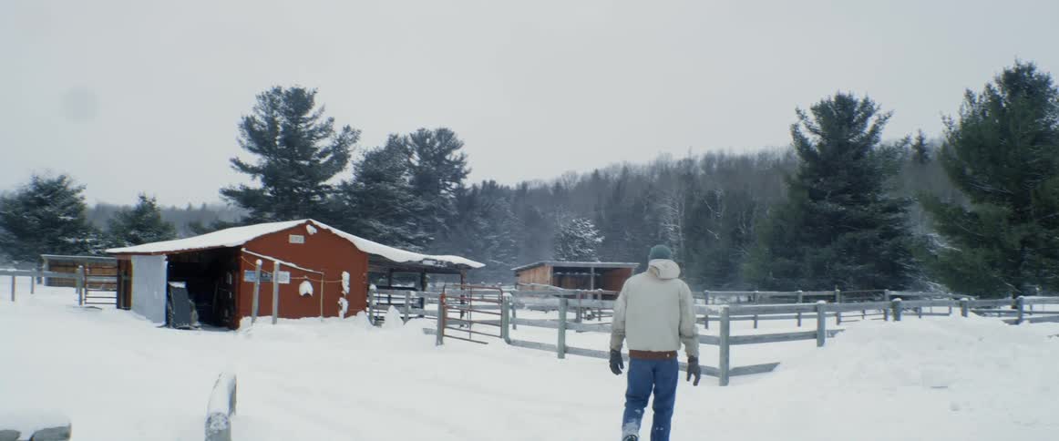 A man walks towards a barn style shelter in a rural area covered with snow
