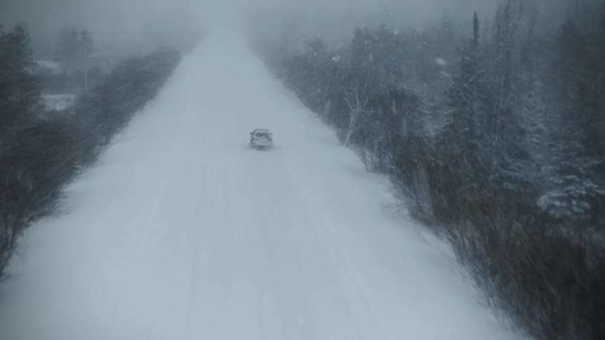 An aerial view of a car driving down a road during a snow storm