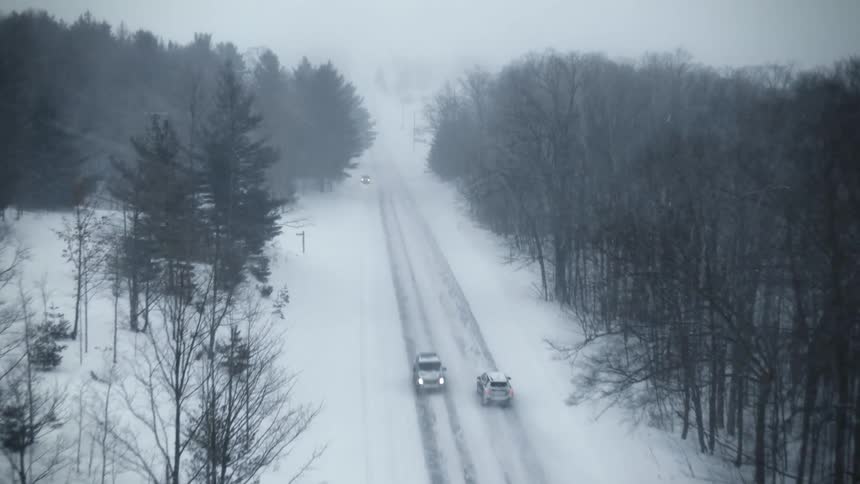 Aerial view of traffic on a snow covered forest road during a blizzard