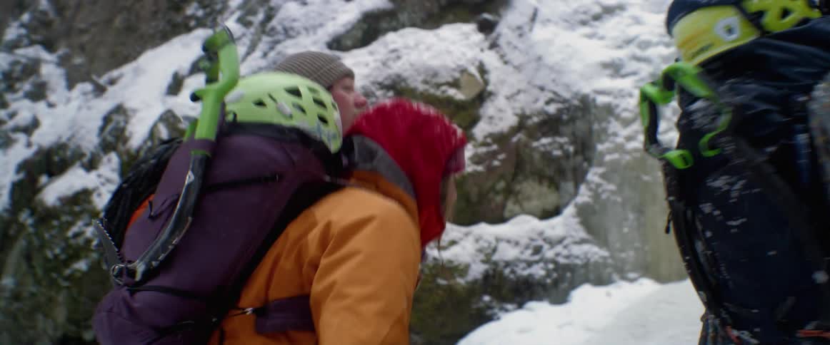 Backpackers stop to look at a waterfall frozen in place as they hike though the forest