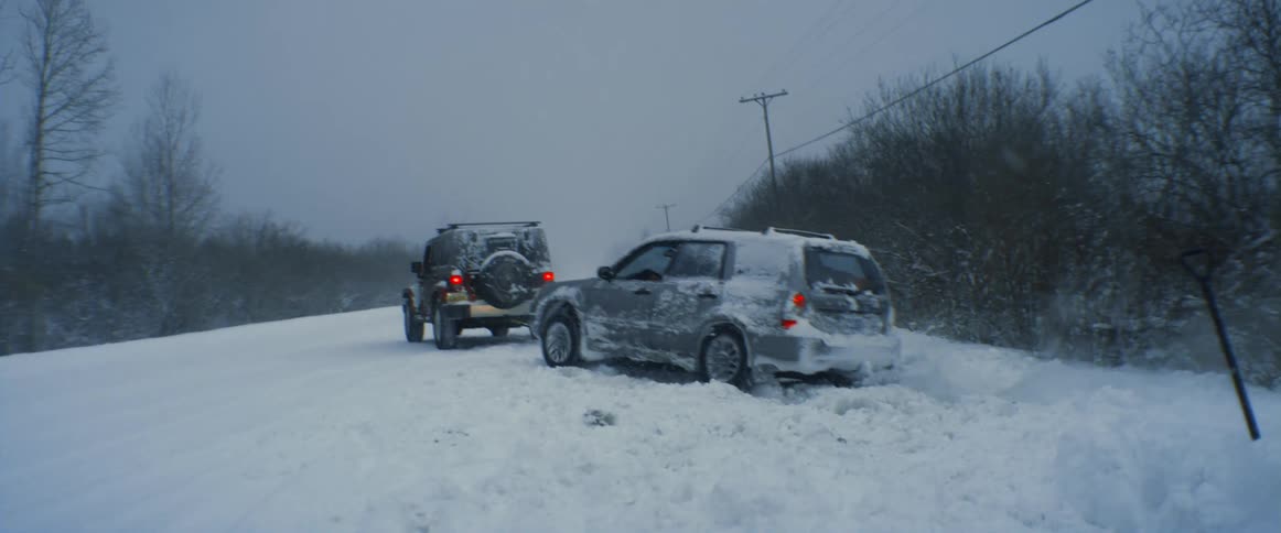 A jeep is pulling another vehicle out of the snow during a blizzard