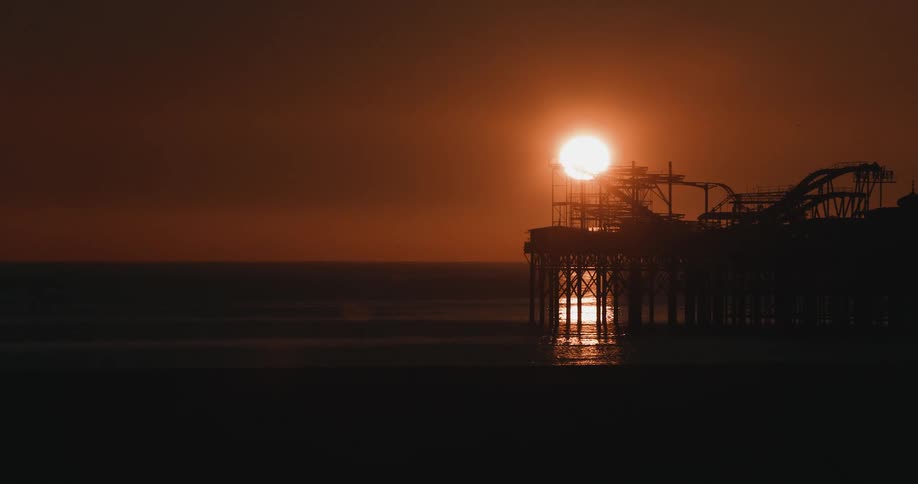 Sun shines in red sky silhouetting amusement park standing on beach