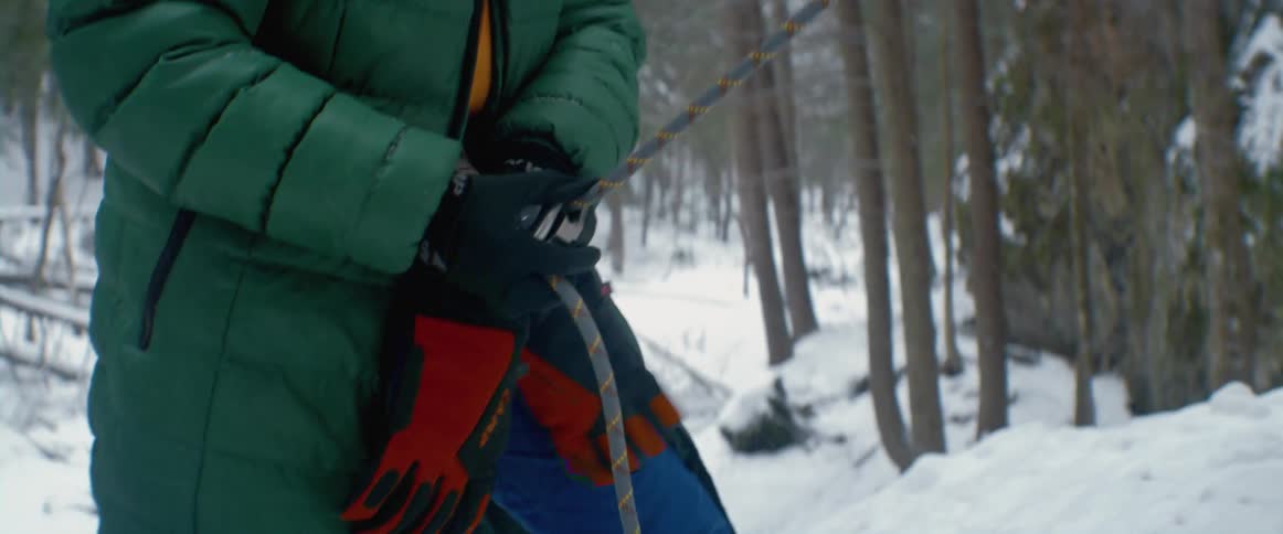 Female climber handles rope as she and another climber stand in snowy forest