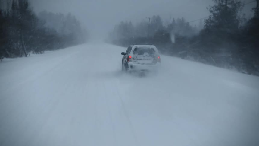Aerial view of a truck traveling on a snow covered forest road during a blizzard