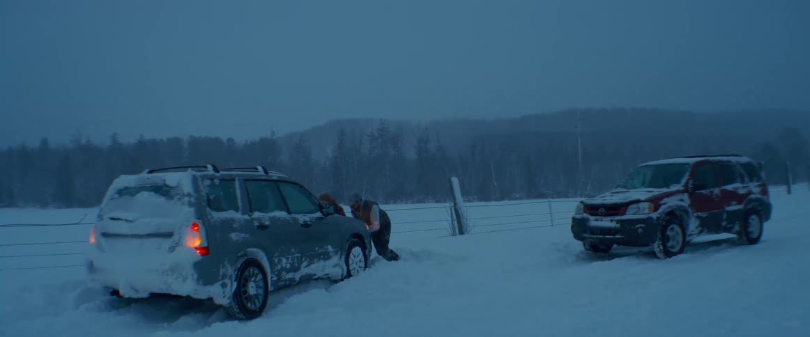 A driver helping others try to push their stuck car out of the snow