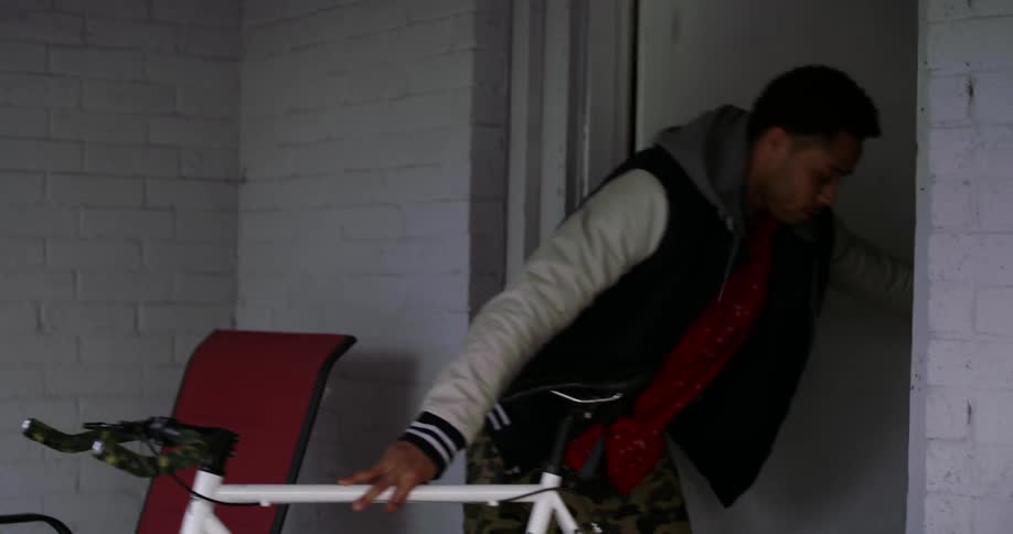 A young man comes through a doorway with a bicycle