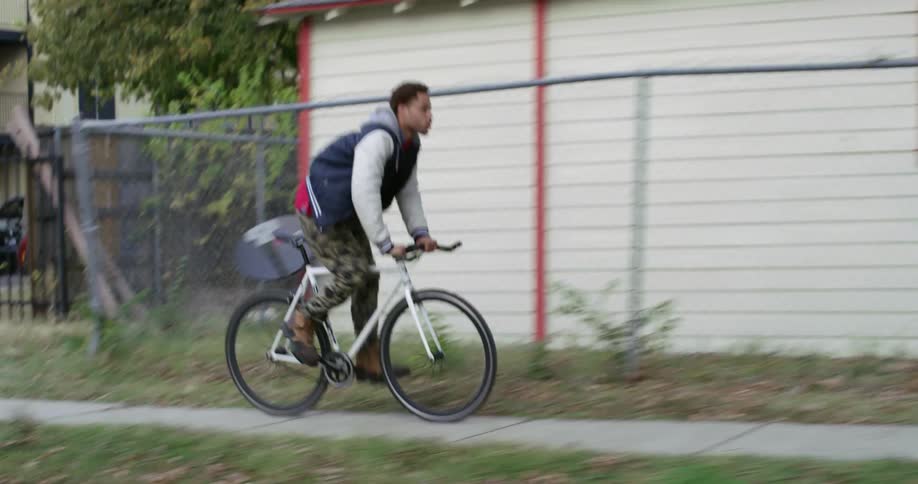A teenager rides a bicycle through a neighborhood during the day