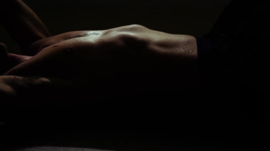 Muscular sweaty shirtless man lying down in the ground at a dark room while heavily breathing