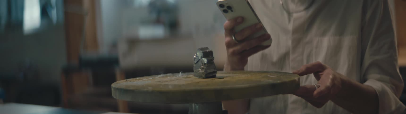 A piece of iron pyrite is on a round turning table and someone is taking a picture of it with their cell phone
