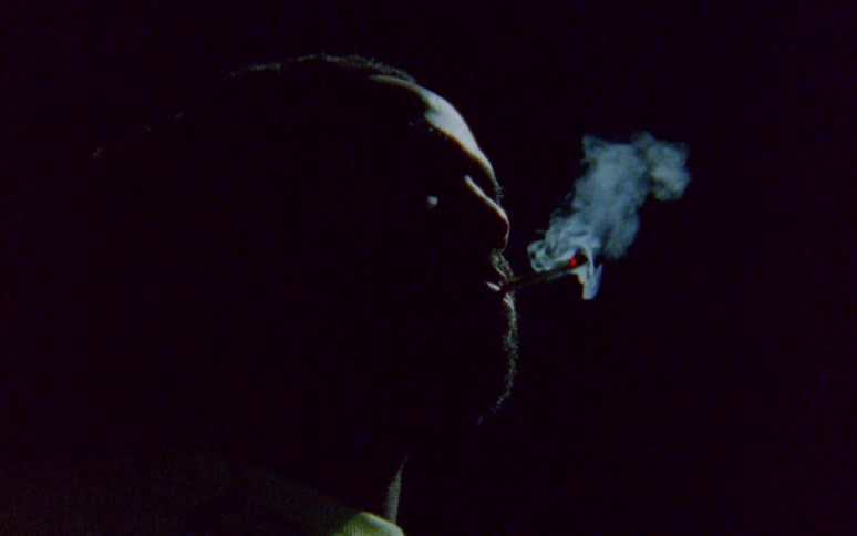 Man with dreadlocks and beard smokes a cigarette in dark