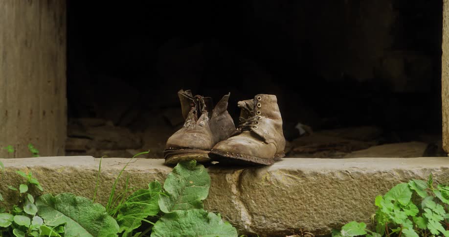 A pair of well worn lace up boots sits on a window ledge