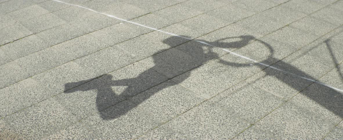 The shadow on concrete of a man hanging from a basketball hoop and doing pull ups