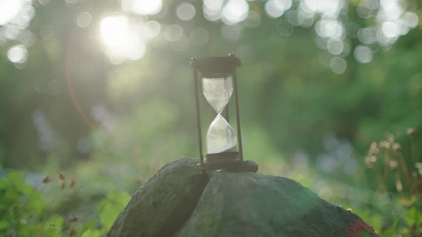 Sand moves through an hourglass as it sits outside on a rock