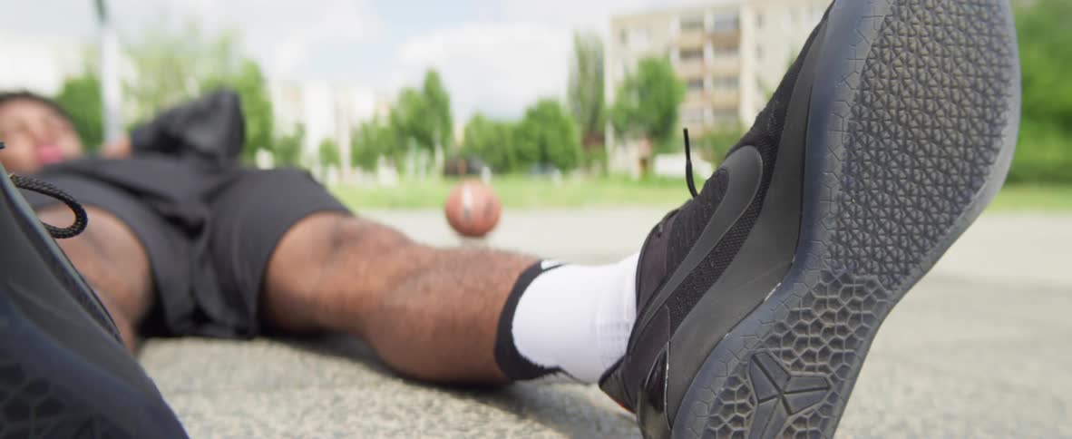 Young black man lying down in the floor at the basketball court wearing black nike shoes and white socks