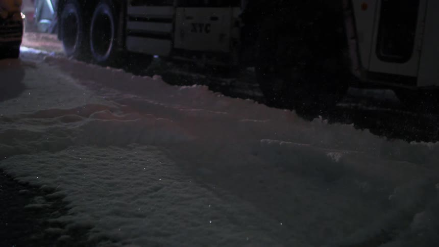 A winter service vehicle plows snow on a city street at night