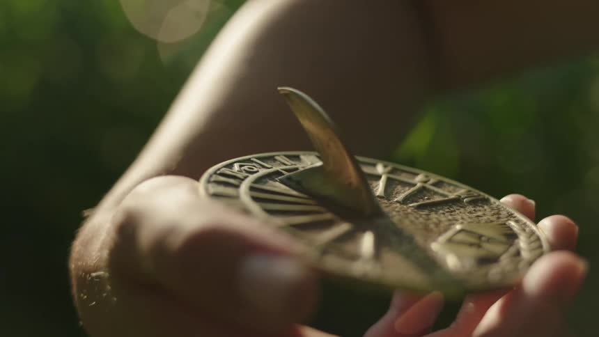 The sun shines brightly on a girls hand holding a sundial