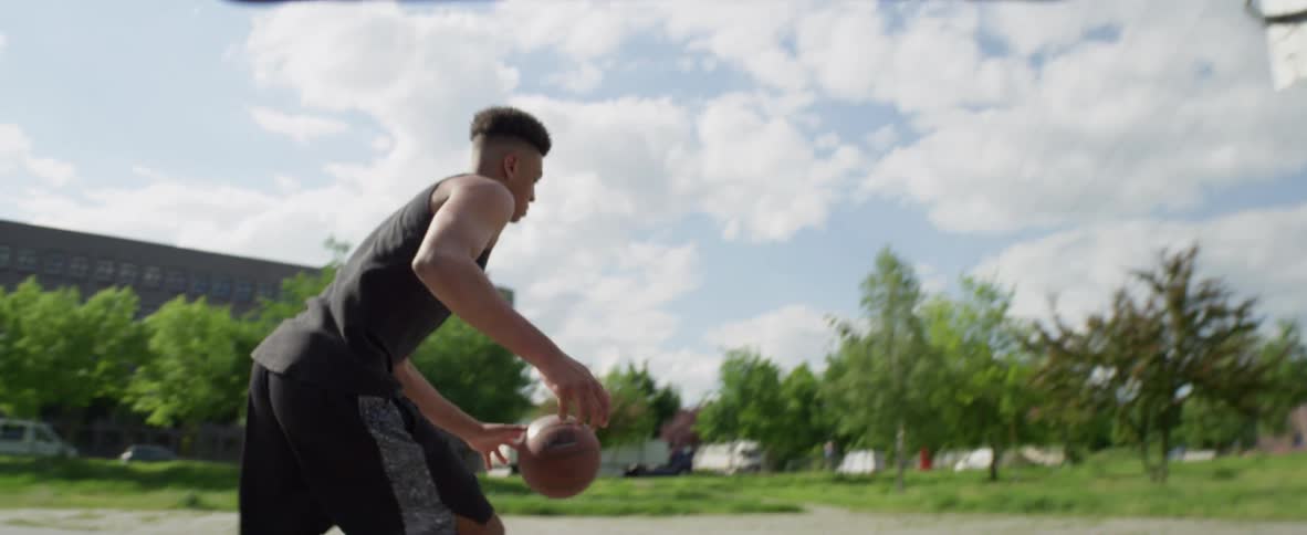 Young black man playing basketball alone at a public basketball court and scoring a point