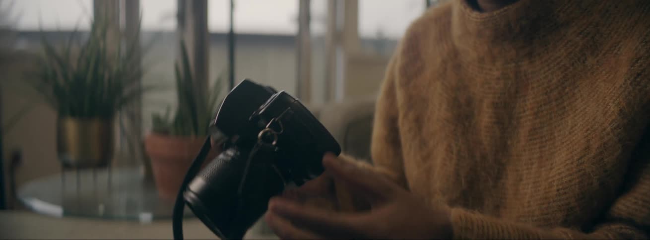 Black woman sitting at a couch wearing a sweater using her camera and taking pictures