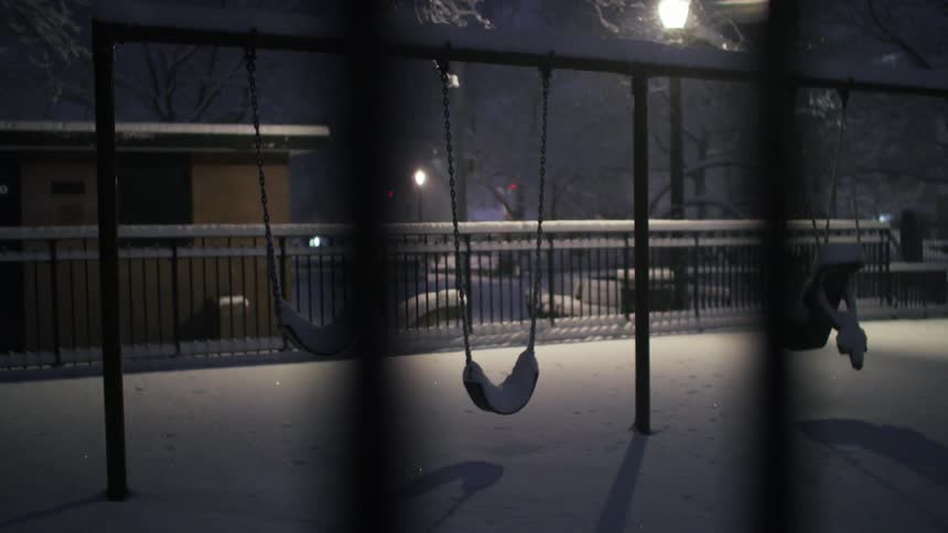 Vacant swings covered in snow at night during a snow storm