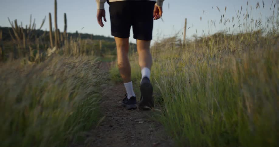 White man walking alone at a dirt trail wearing black shoes white socks and black shorts