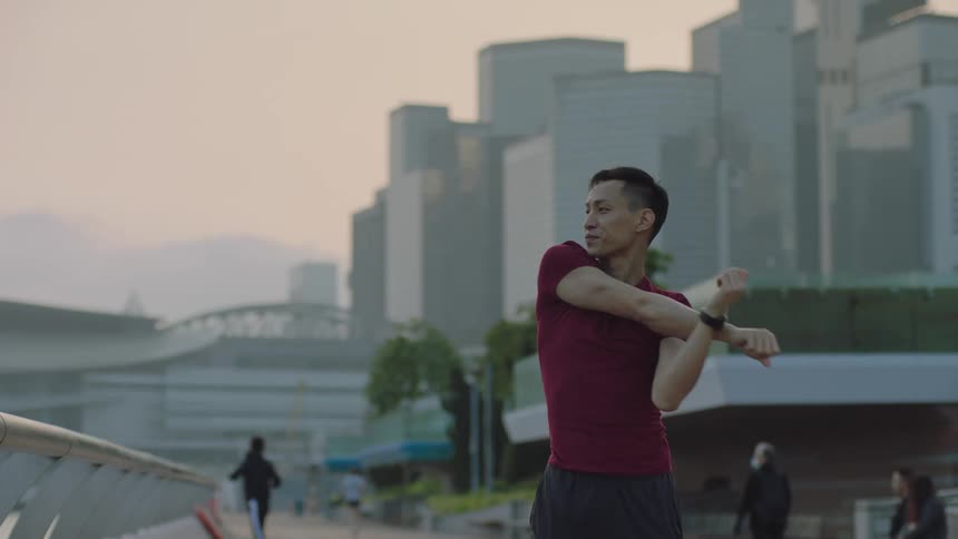 Young asian man wearing fitness clothing streching and warming up and then jogging at a public space in a big city