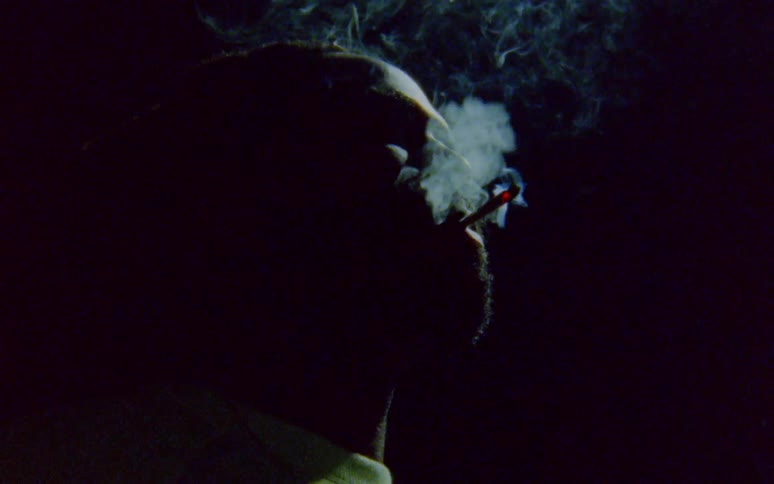 Man with dreadlocks and beard smokes a cigarette in dark