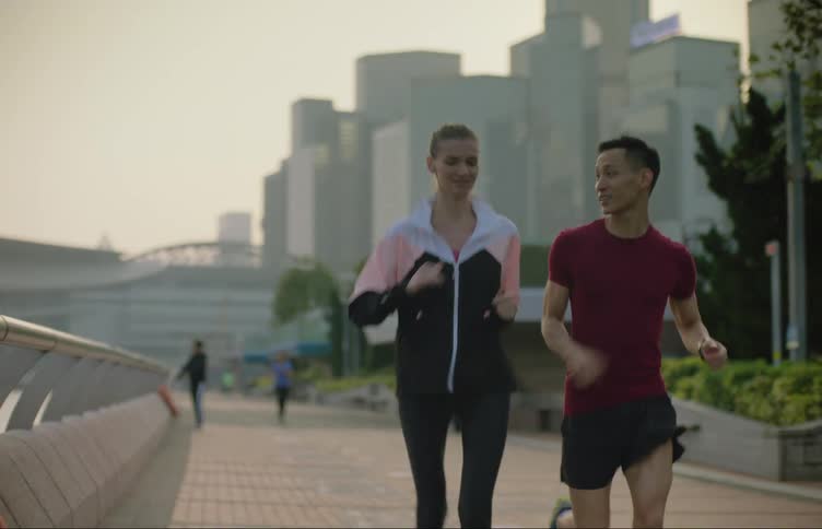 A man and woman run together on a city pedestrian sidewalk