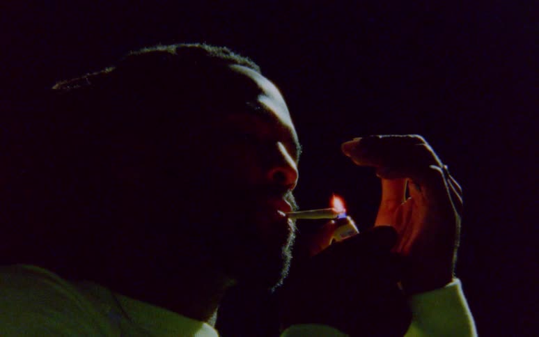 A man lights up a marijuana joint with a light and blows smoke