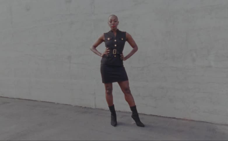 A woman stands with her hands on her hips in front of a wall