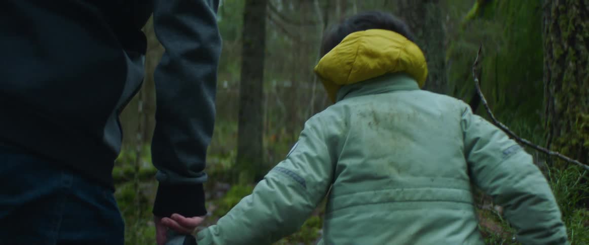 Father and son wearing coats holding hands and walking together in the middle of a forest