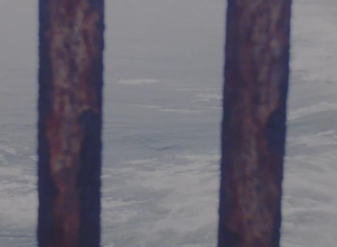 View of an ocean wave crashing on a beach near a pier in the daytime