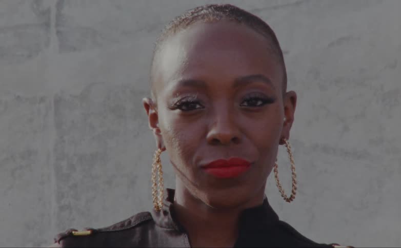 A black woman with long lashes and red lips smirks as she looks straight ahead