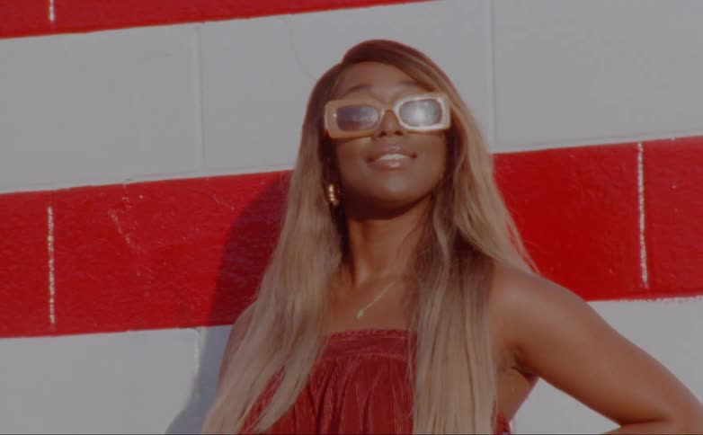 A black woman with long hair smiles as she poses in front of a striped wall