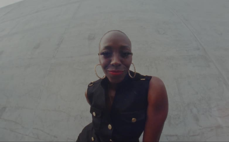 Balde female model with hoop earrings and black dress looks down at camara shaking her head
