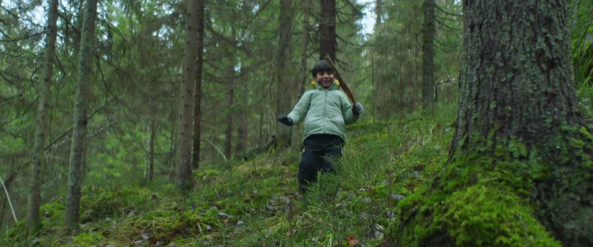 Young boy wearing gloves and jacket playing with a stick on a forest at daytime