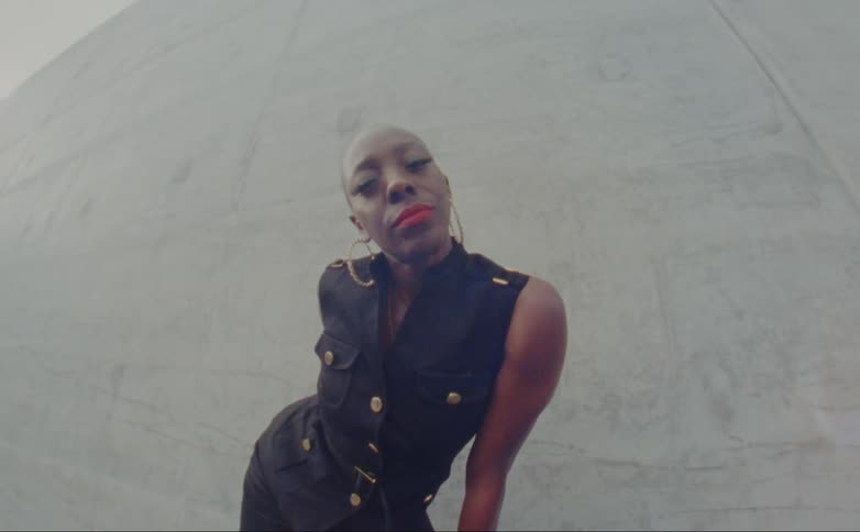 A black woman wearing large hoop earrings poses by the concrete wall