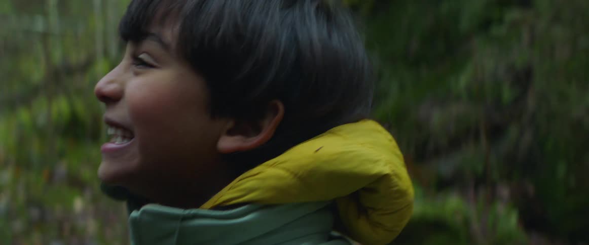 A boy laughs as he stands in the woods