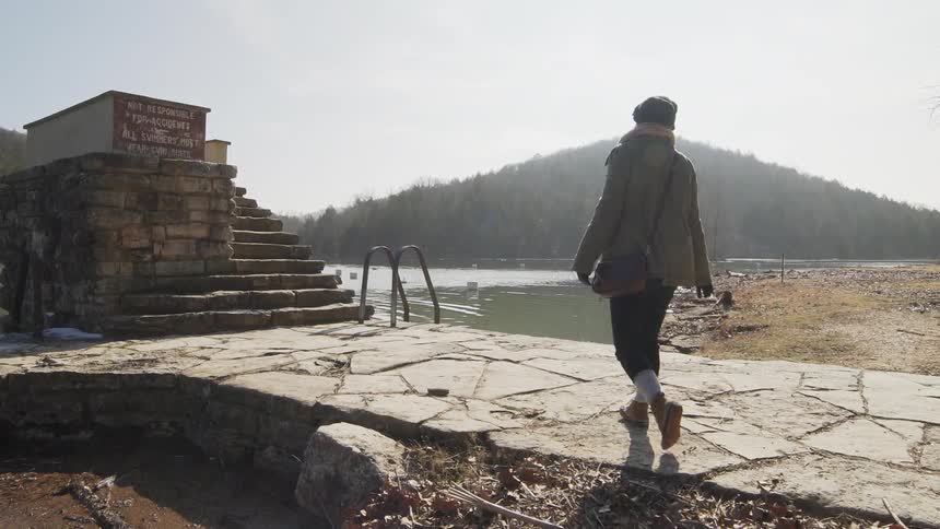 Person walks alongside a muddy-looking lake